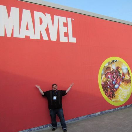 C. B. Cebulski is standing in front of huge Marvel board.